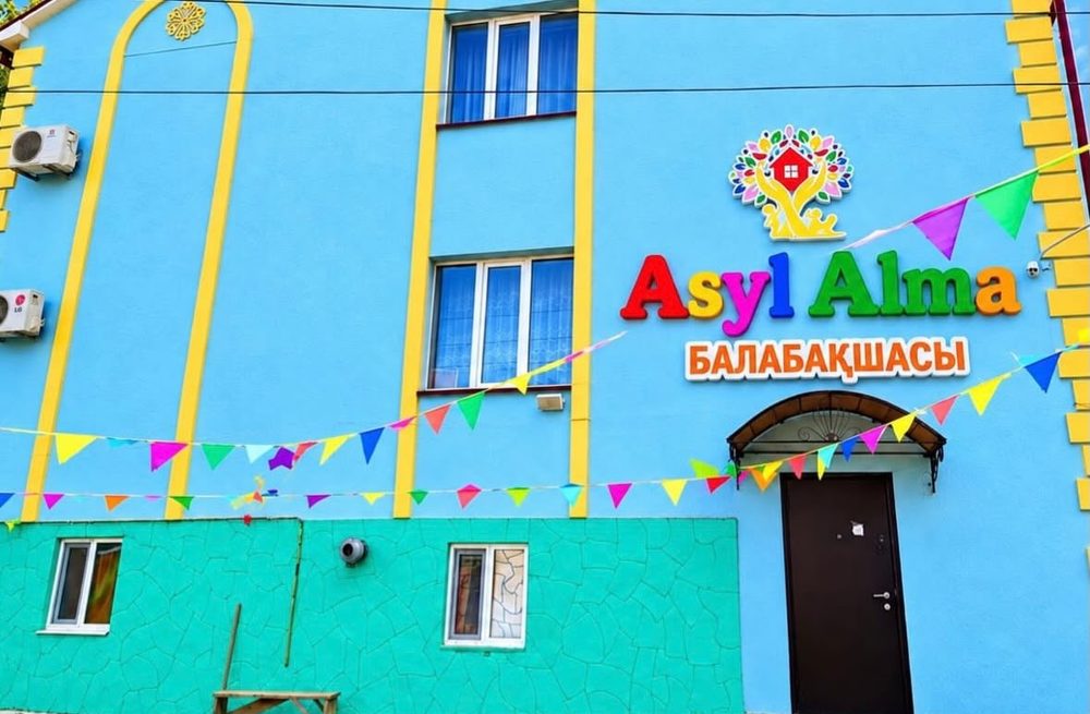 Здание детского сада Асыл-Алма с яркой вывеской и цветными флажками